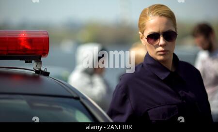 Concentrés femme officier debout près de voiture de police, d'un accident sur l'arrière-plan Banque D'Images