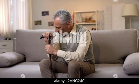 L'homme a pris sa retraite avec la canne assis sur un canapé, la solitude et la dépression, problèmes Banque D'Images