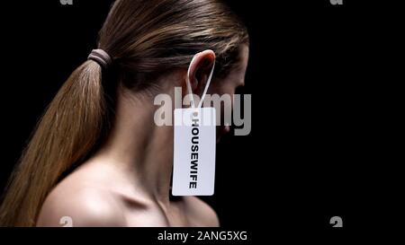 Dame avec étiquette ménagère sur oreille sur fond sombre, place des femmes, le sexisme Banque D'Images