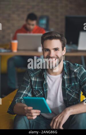 Cheerful barbu assis avec le comprimé dans la main Banque D'Images