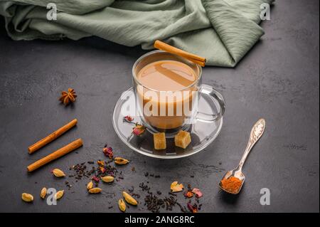 Thé traditionnel indien masala chai. La cannelle, l'anis, la cardamome, le sucre à côté d'un fond texturé noir Banque D'Images