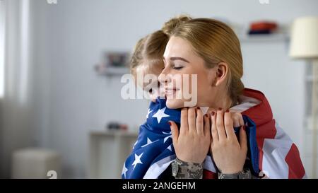 Little daughter hugging soldier avec nous drapeau, heureux avec homecoming Banque D'Images