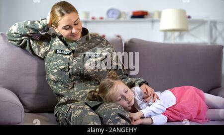 Fille dormir sur les genoux des mères soldat américain, reposant sur un canapé à la maison Banque D'Images