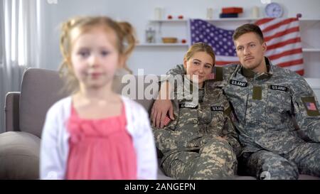 Les parents joyeux en uniforme militaire admirant petite fille looking at camera Banque D'Images