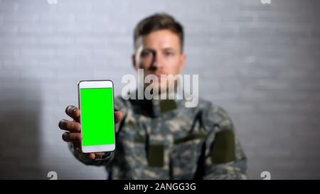 Femme soldat en uniforme montrant smartphone avec appareil photo à écran vert, l'app Banque D'Images