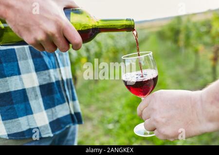 Vigneron verse le vin rouge d'une bouteille de vin dans un verre de vin dans une main Banque D'Images