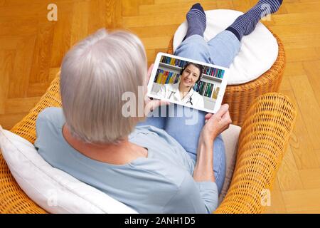 Concept de télémédecine, vieille femme avec tablette pc lors d'une consultation en ligne avec son médecin dans sa salle de séjour. Banque D'Images