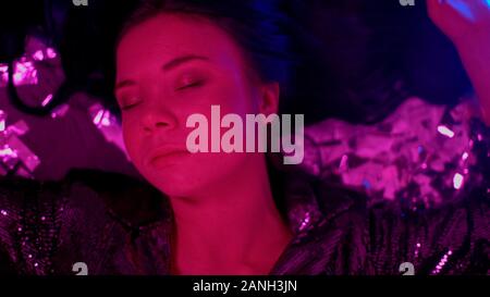 Young woman lying on floor parmi les confettis dans night club, problème de dépendance Banque D'Images