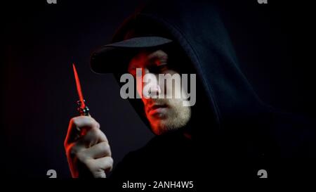 Angry Man in hoodie holding knife sur le lieu de crime, fond sombre, preuve Banque D'Images