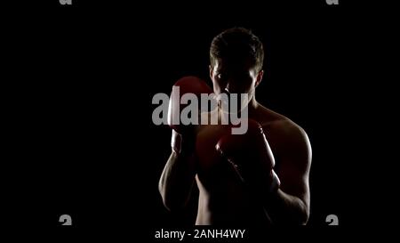 Strong man in boxing gloves prépare à combattre, de formation en salle de sport fond noir Banque D'Images