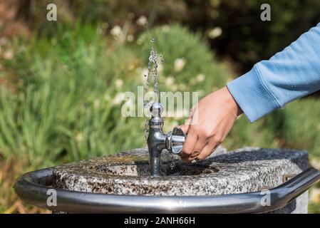 Une main tenant une fontaine publique de boisson. L'eau qui s'écoule éclabousse vers le haut. Banque D'Images