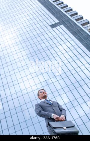 Business man with briefcase debout sur l'herbe près de tall office building Banque D'Images