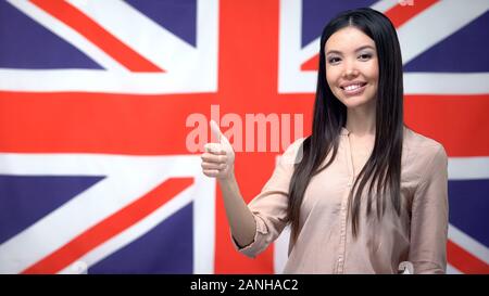 Belle femme showing thumbs-up contre le drapeau britannique, l'arrière-plan template Banque D'Images