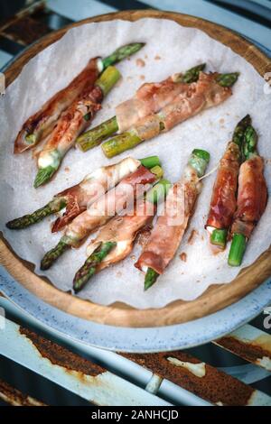 Buffet de plats - jambon de Parme et asperges enrobées de mozzerella servies sur une assiette sur un banc de pique-nique rose. Pose plate Banque D'Images