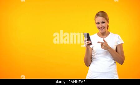 Happy young woman pointing at smartphone part, crédit facile, application en ligne Banque D'Images