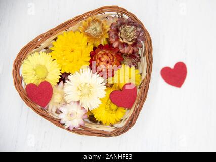 En forme de coeur un panier plein de fleurs séchées et quelques coeurs rouges Banque D'Images