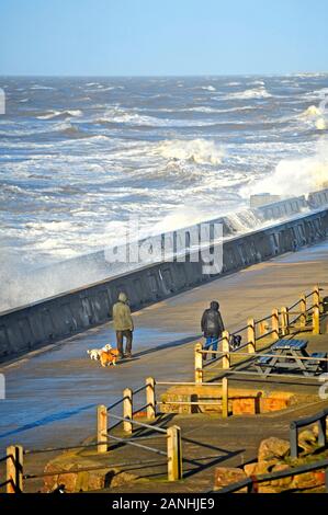 Couple walking dogs comme des vagues se briser sur la digue à marée haute ou la tempête à Blackpool, Royaume-Uni Banque D'Images