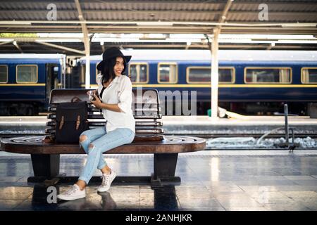 Les cheveux ondulés femme assis sur banc en bois à plate-forme du train prise en main de l'appareil et revenir. Banque D'Images