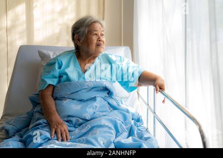 Personnes âgées Les patients déprimés asiatique femme couchée sur le lit en regardant par la fenêtre à l'hôpital. Femme âgée patients est heureux récupéré de la maladie. Banque D'Images