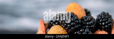 Bannière avec les framboises noires et jaunes dans un panier en bois gris sur fond de bois. Close up. Banque D'Images