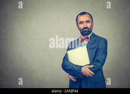 Closeup portrait of a handsome bearded man holding laptop looking at camera vous grave. Course mixte modèle barbu isolé sur mur studio gris background Banque D'Images