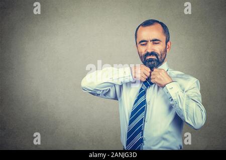 Closeup portrait of tired businessman taking off sa cravate. Course mixte modèle barbu isolé sur fond gris mur studio avec copie espace. Horizo Banque D'Images
