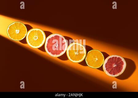 Les agrumes, réduit de moitié, dans une rangée, en plein soleil, sur un fond de couleur de lave. Voir ci-dessus de l'été fruits tropicaux. Les oranges et les pamplemousses frais Banque D'Images