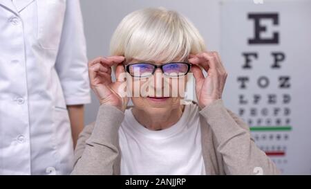 Senior woman wearing nouvelles lunettes en magasin d'optique, le choix du matériel, la santé Banque D'Images