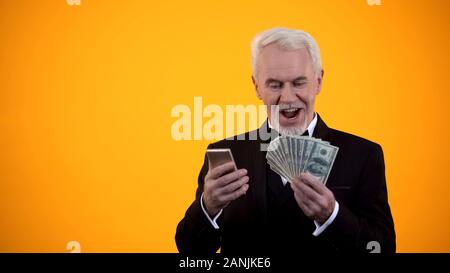 Happy retired man in suit online parier sur téléphone cellulaire, réjouissez-prix en argent Banque D'Images