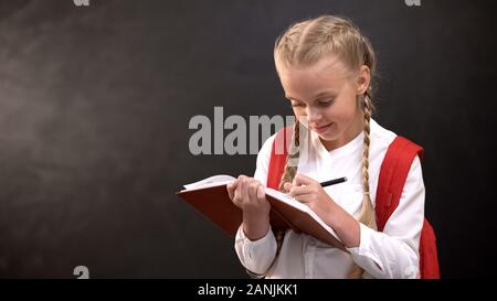 Petite lycéenne écrit dans l'ordinateur portable, faire ses devoirs contre tableau noir Banque D'Images