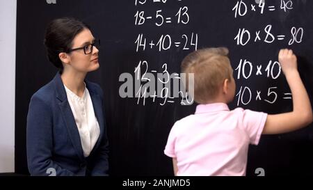 Smiling teacher fier de petit garçon de problèmes exemples mathématiques, école privée Banque D'Images