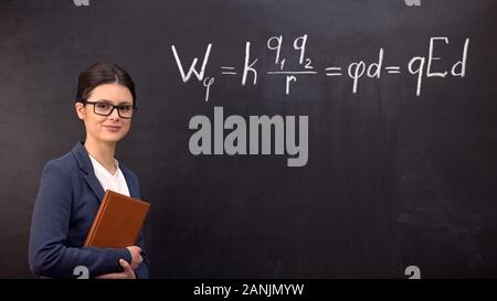 Les jeunes enseignants astucieux debout près de tableau noir et à la formule à l'appareil photo, Banque D'Images
