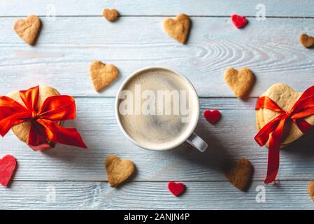 Tasse de café et un joli cadeau de cookies attachées avec du ruban rouge en forme de cœur sur un fond en bois bleu. Cadeaux de la saint Valentin romantique Banque D'Images