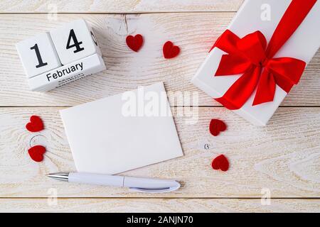 Carte de vœux vide, boîte-cadeau avec ruban arc et calendrier perpétuel avec date 14 février sur une surface texturée en bois blanc. L'amour et des sentiments concept. Banque D'Images