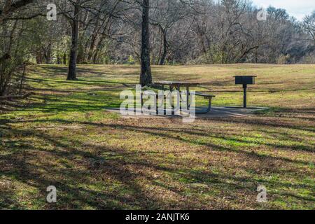 Une table de pique-nique et barbecue sous les arbres ombragés sur un socle de ciment entouré d'arbres et l'herbe dans un parc dans la forêt par une belle journée ensoleillée dans Banque D'Images