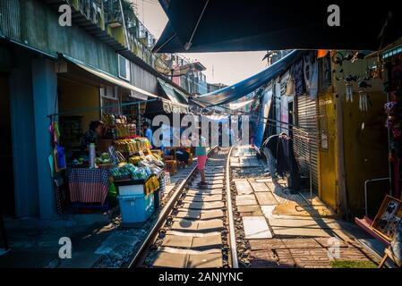 Mae Klong/Thailand-08December2019: Gare de Mae Klong avec voies et train passant par le marché quotidien avec des vendeurs vendant tout. Banque D'Images