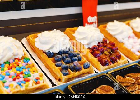 Gaufres Belges street food avec différentes garnitures, du fruits, des bonbons, de la crème fouettée. Vitrine pâtisserie gaufres belges de divers types. Stock Photo Banque D'Images