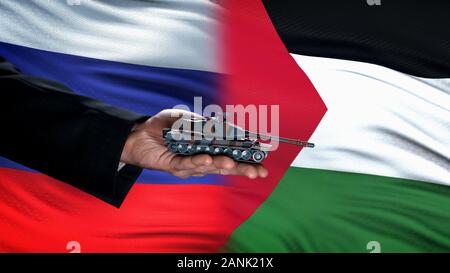 Deux hand holding toy réservoir contre la Russie et la Palestine flag background Banque D'Images