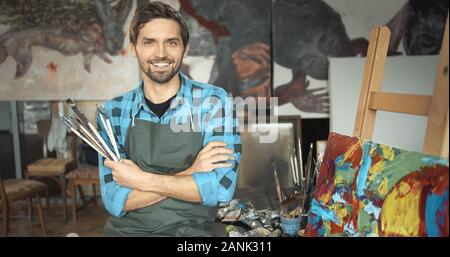 Portrait of young smiling artiste posant avec les pinceaux dans son studio loft Banque D'Images