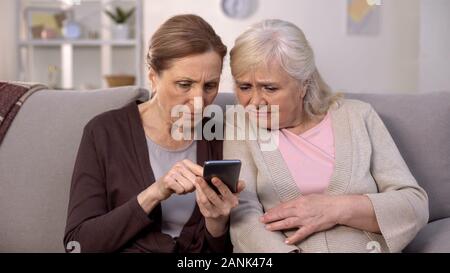 Deux femmes matures l'utilisation d'apprentissage séance canapé d'accueil du smartphone, la technologie de la vieillesse Banque D'Images