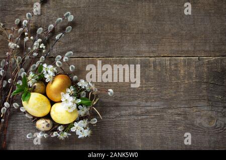 Golden œufs de Pâques colorés dans un nid avec des branches de saule et de fleurs de printemps sur un fond de bois gris. Vue supérieure de la télévision mise de fond. Spa de copie Banque D'Images