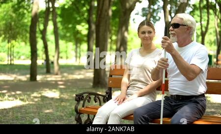 Femme positive et un homme aveugle, passer du temps sur le banc de parc, l'appui et les soins Banque D'Images