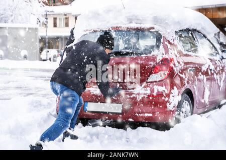 Homme poussant une voiture prise dans la neige après les fortes chutes de neige Banque D'Images