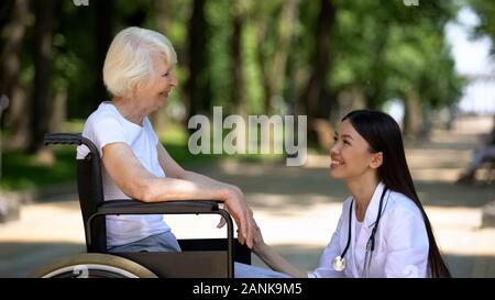 Smiling nurse talking with disabled elderly woman in park, centre de réadaptation Banque D'Images