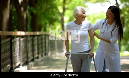 Femme médecin aidant femme âgée avec déambulateur, parc de l'hôpital, à l'extérieur Banque D'Images