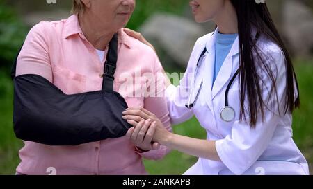 Young smiling doctor en prenant soin de vieille femme avec bras sling, chirurgien traumatologie Banque D'Images