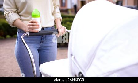 Jeune mère tenant une bouteille de lait se balançant la pram, la nutrition infantile, de soins de santé pour enfants Banque D'Images