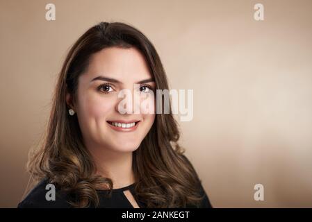 Portrait of smiling femme latine sur fond marron studio Banque D'Images