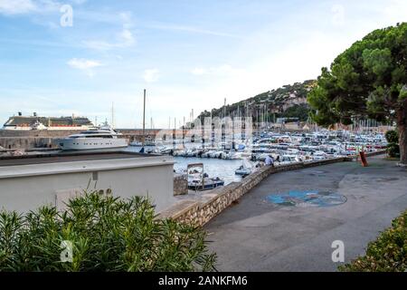 Une jeune personne assise seule sur un mur de pierre le long de la marina au coucher du soleil sur un bateau de croisière au port sur la côte d'Azur. Banque D'Images