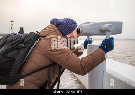 L'homme avec un sac à dos, qui observe avec intérêt dans la tour spectateur, debout sur la promenade, sur la toile de fond de la mer. Banque D'Images